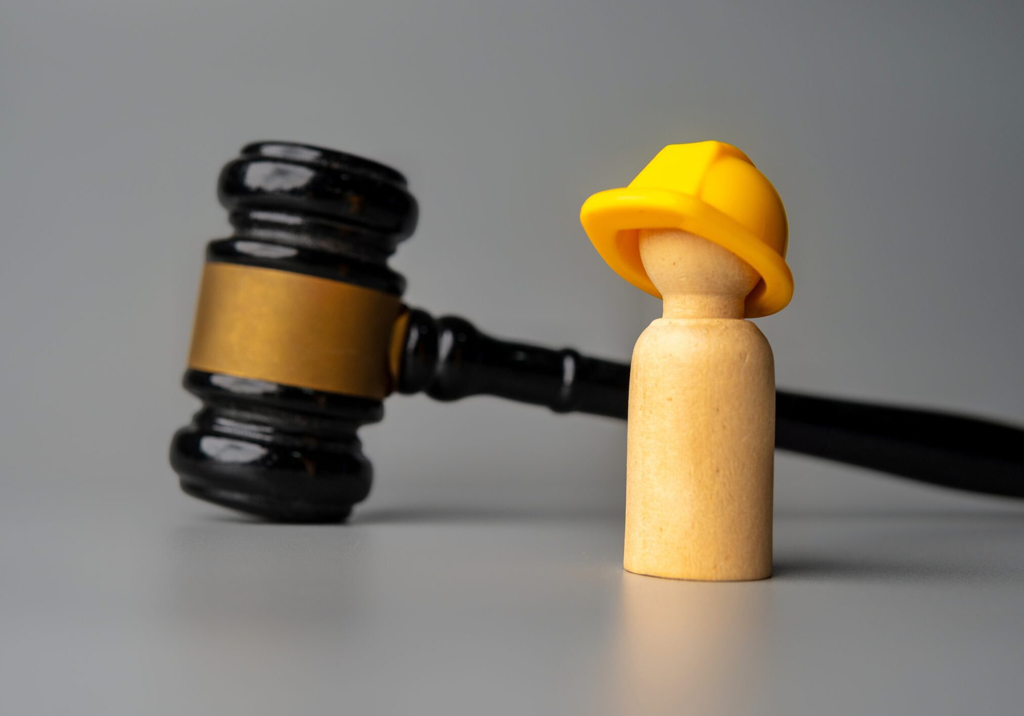 A wooden figure wearing a yellow firefighter helmet beside a judge's gavel.